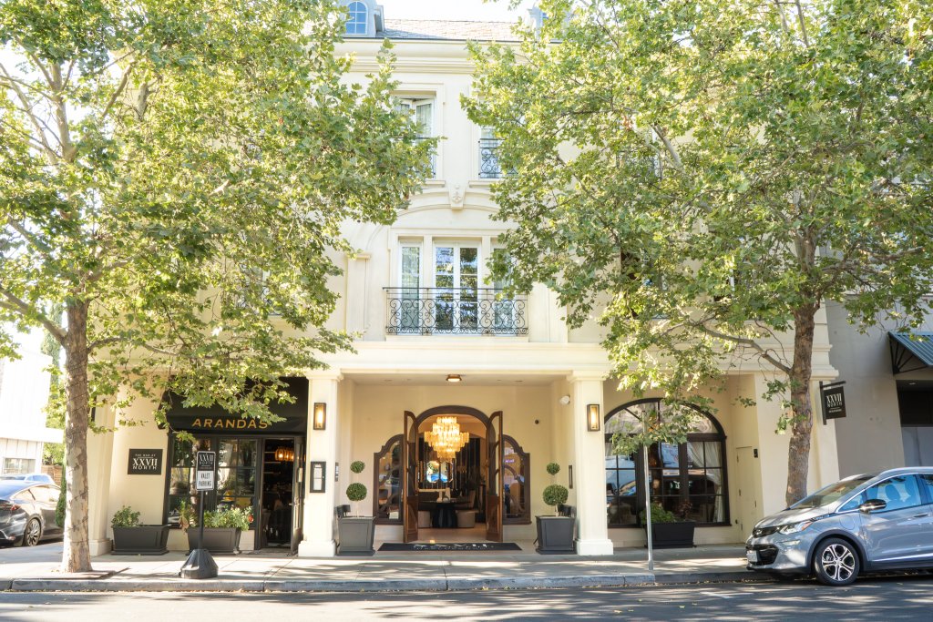 A three-story building with a grand entrance, surrounded by lush green trees and a parked car in Healdsburg, California.
