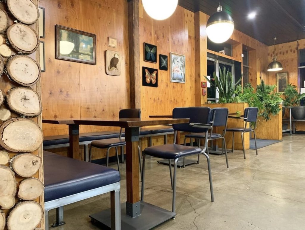 A cozy cafe with wooden walls adorned with framed art, featuring tables, chairs, and a bench with blue cushions, illuminated by hanging pendant lights in Healdsburg, California.