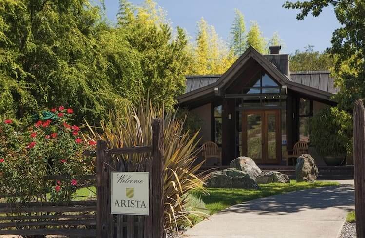 A quaint, modern house nestled among lush greenery with a welcoming sign reading 'Welcome to Arista' in Healdsburg, California.