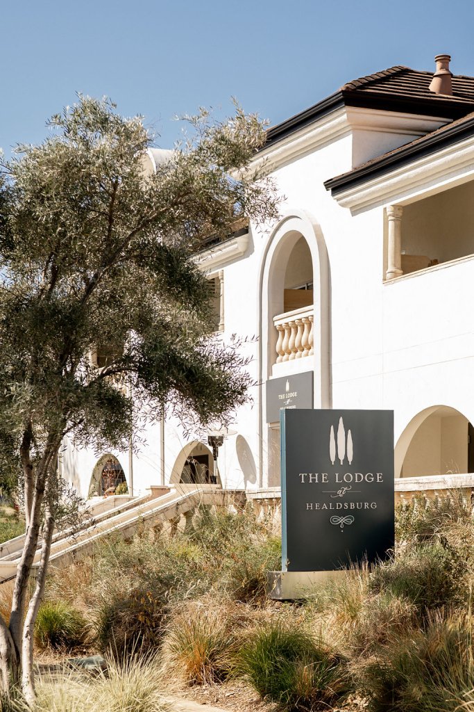 A white Mediterranean-style building with arched windows and balconies, surrounded by lush greenery and a sign reading 'The Lodge at Healdsburg' in Healdsburg, California.