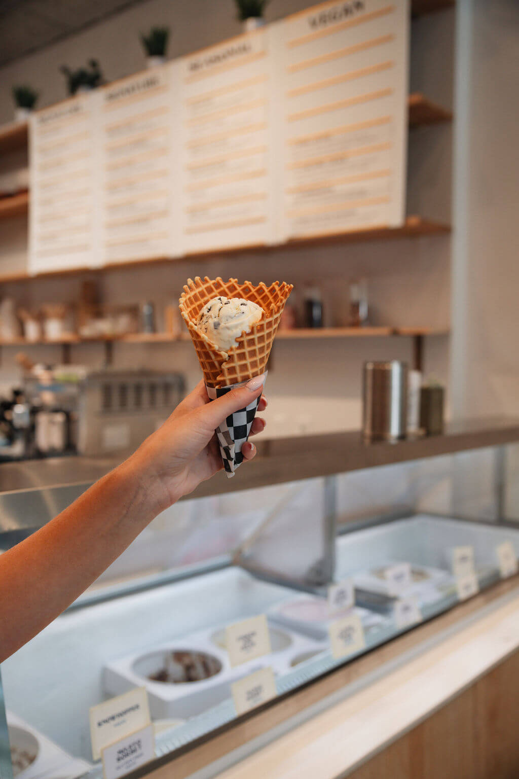 Angela's Organic Ice Cream A hand holds a waffle cone filled with ice cream in a modern ice cream shop in Healdsburg, California.