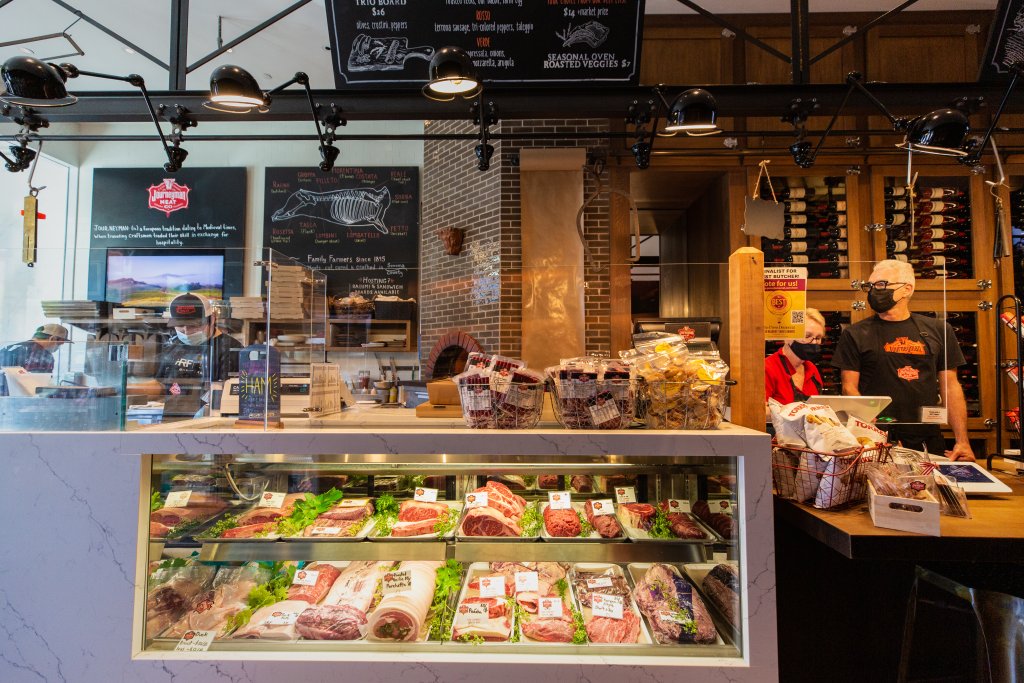 A butcher shop counter displays a variety of meats and cheeses behind glass, with staff wearing masks in Healdsburg, California.