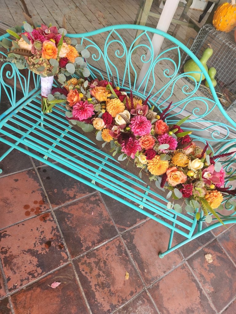 A vibrant floral arrangement of roses, dahlias, and other colorful flowers adorns a turquoise metal bench in Healdsburg, California.