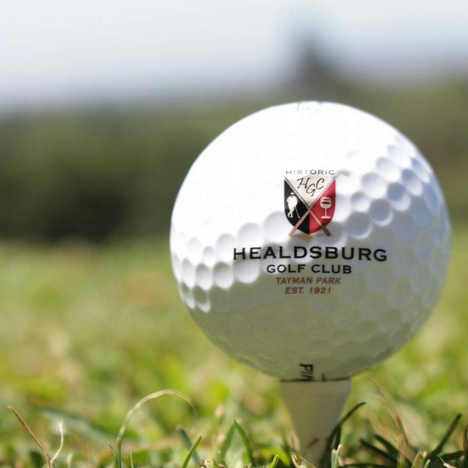 A white golf ball with the Healdsburg Golf Club logo sits on a tee in the grass in Healdsburg, California.