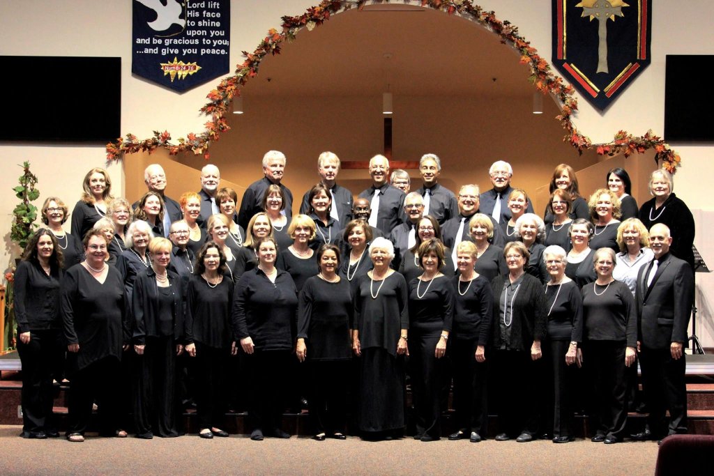 A large choir of diverse ages and genders dressed in black performs in a church setting in Healdsburg, California.