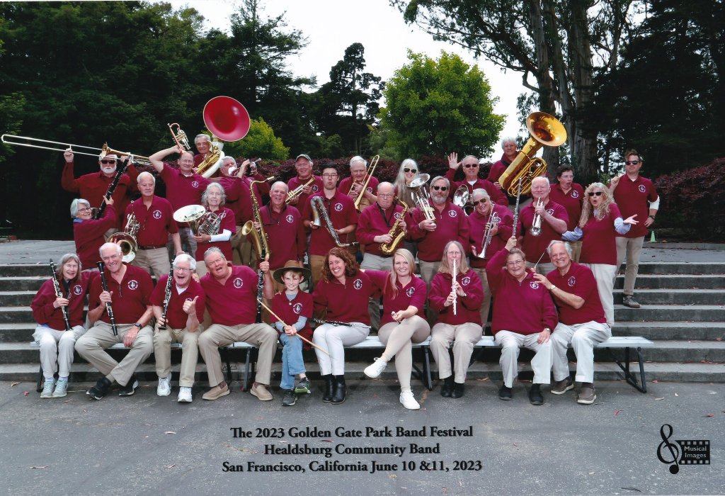A large group of musicians in red shirts pose together with their instruments on stone steps in Healdsburg, California.