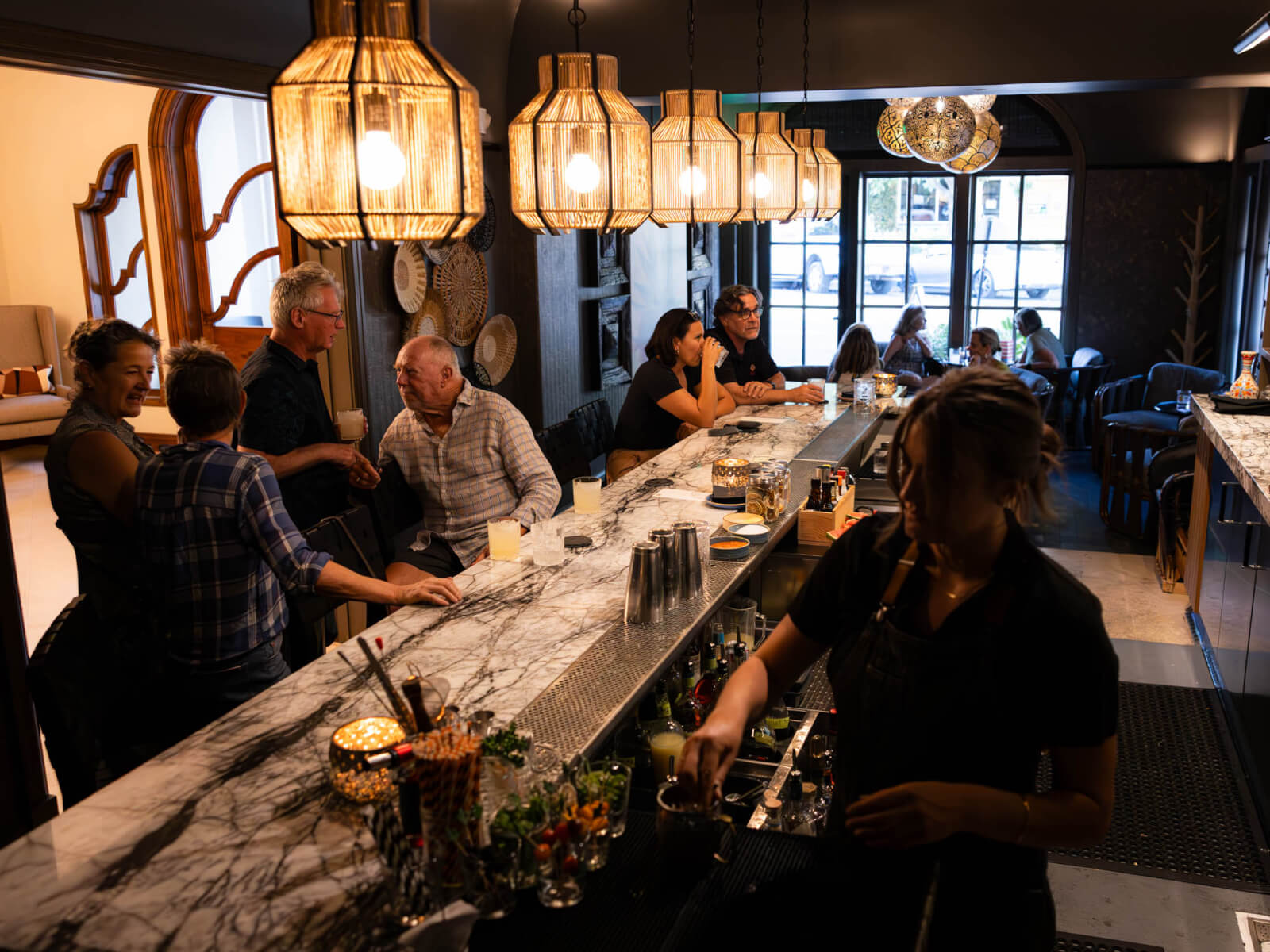 Arandas Patrons enjoy drinks at a dimly lit bar with a marble counter and hanging lanterns in Healdsburg, California.