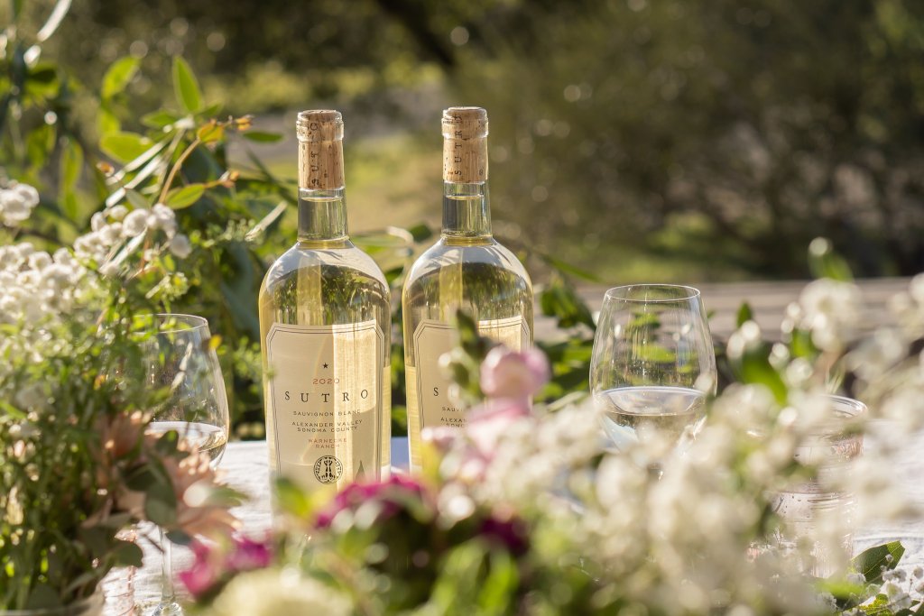 Two bottles of Sutro Sauvignon Blanc wine with corks, two filled wine glasses, and a vase of white flowers on a table in Healdsburg, California.