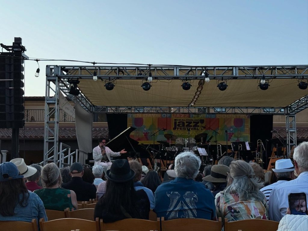 Outdoor jazz concert with pianist and orchestra on stage, audience seated in rows of chairs in Healdsburg, California.