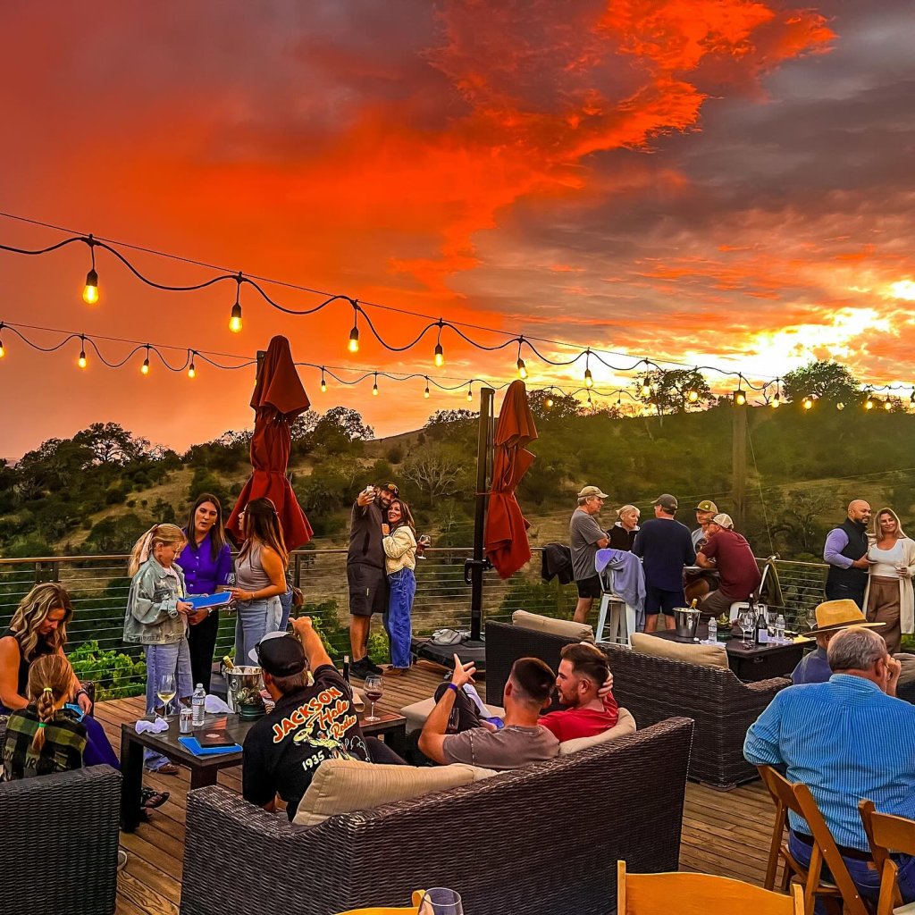 A group of people enjoying a sunset gathering on a rooftop deck with string lights in Healdsburg, California.