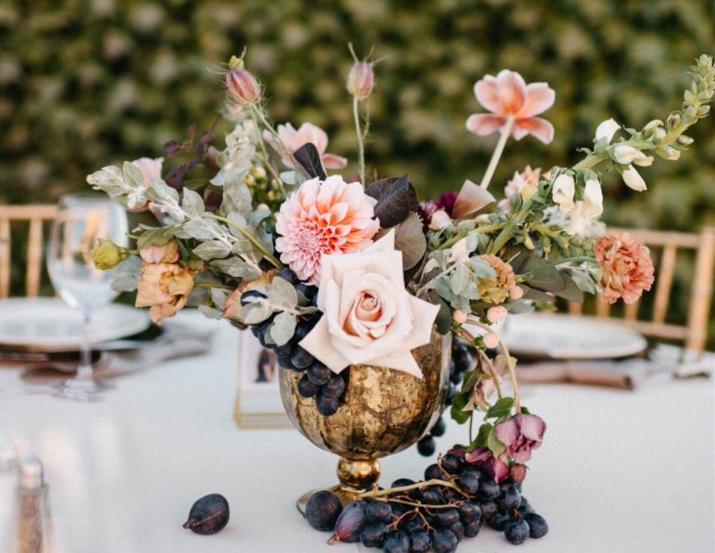A golden vase filled with a bouquet of pink roses, dahlias, and grapes on a table in Healdsburg, California.