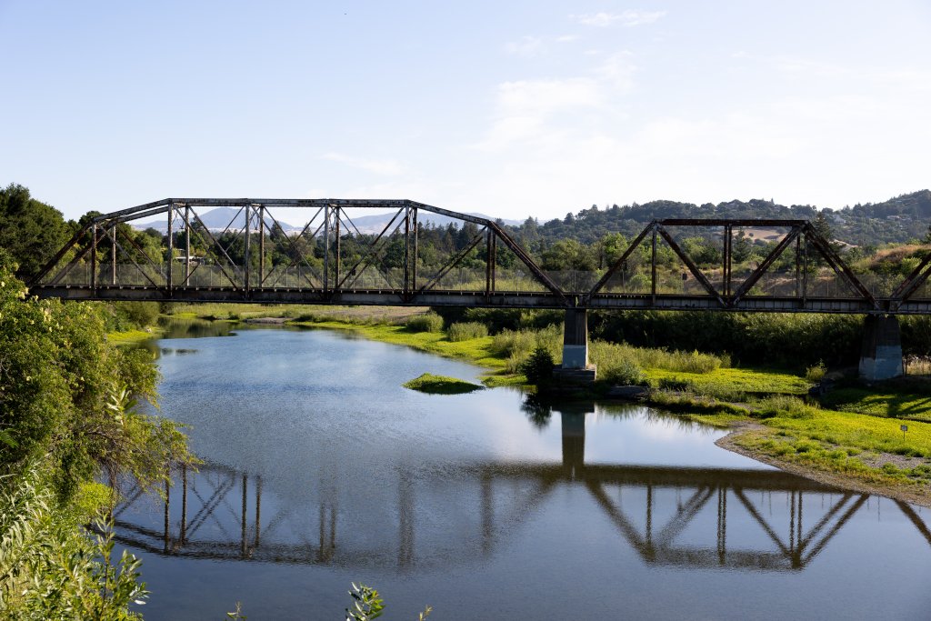 A rustic metal truss bridge spans a calm river, reflecting in the water below in Healdsburg, California.