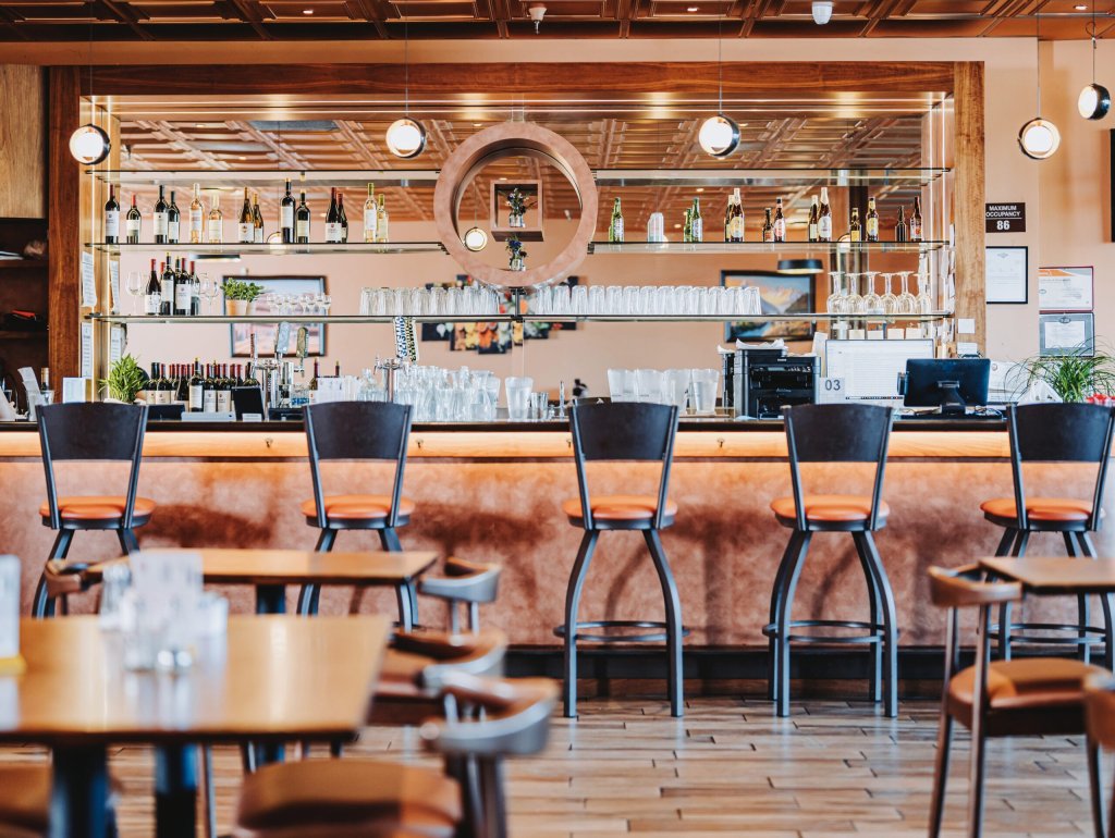 A modern restaurant bar with wooden decor, orange stools, and a variety of wine bottles displayed in Healdsburg, California.