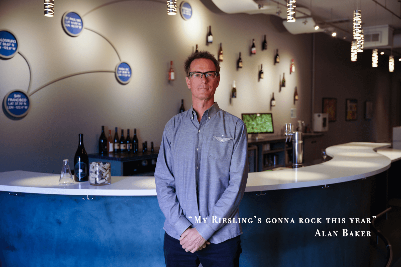 Man stands at bar with wine bottles and tasting notes on wall in Healdsburg, California.