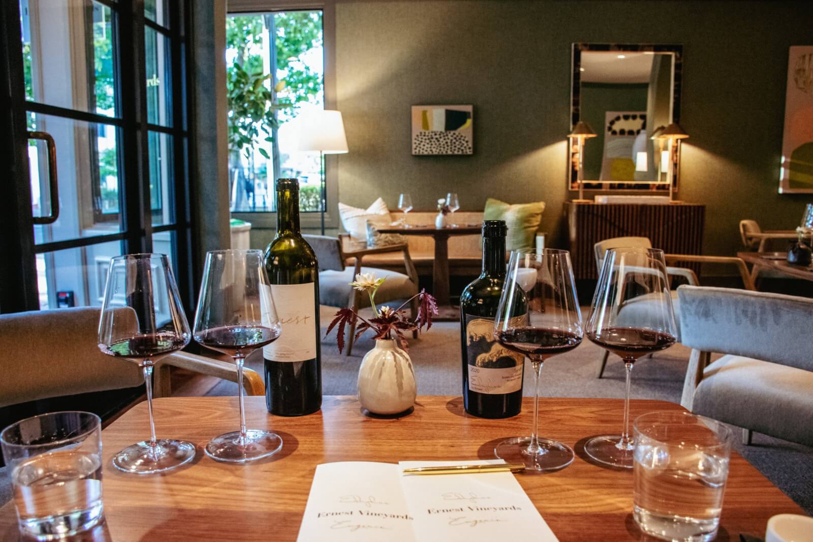 Ernest Vineyards A cozy tasting room with wine bottles, glasses, and a menu on a wooden table in Healdsburg, California.