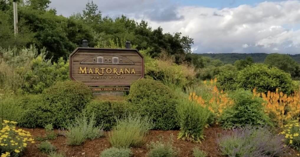 A wooden sign for Martorana Family Winery stands amidst lush greenery and vibrant wildflowers in a picturesque vineyard setting in Healdsburg, California.