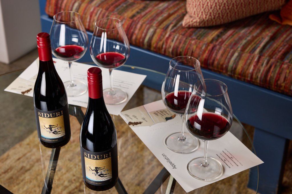 Four glasses of red wine and two bottles of Siduri wine on a glass table in Healdsburg, California.