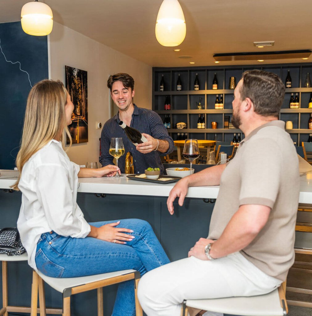 Three people enjoying wine and conversation at a stylish bar with a well-stocked wine rack in Healdsburg, California.