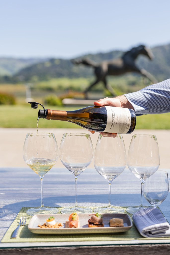 A hand pours white wine into four glasses on a table with food and napkins in Healdsburg, California.