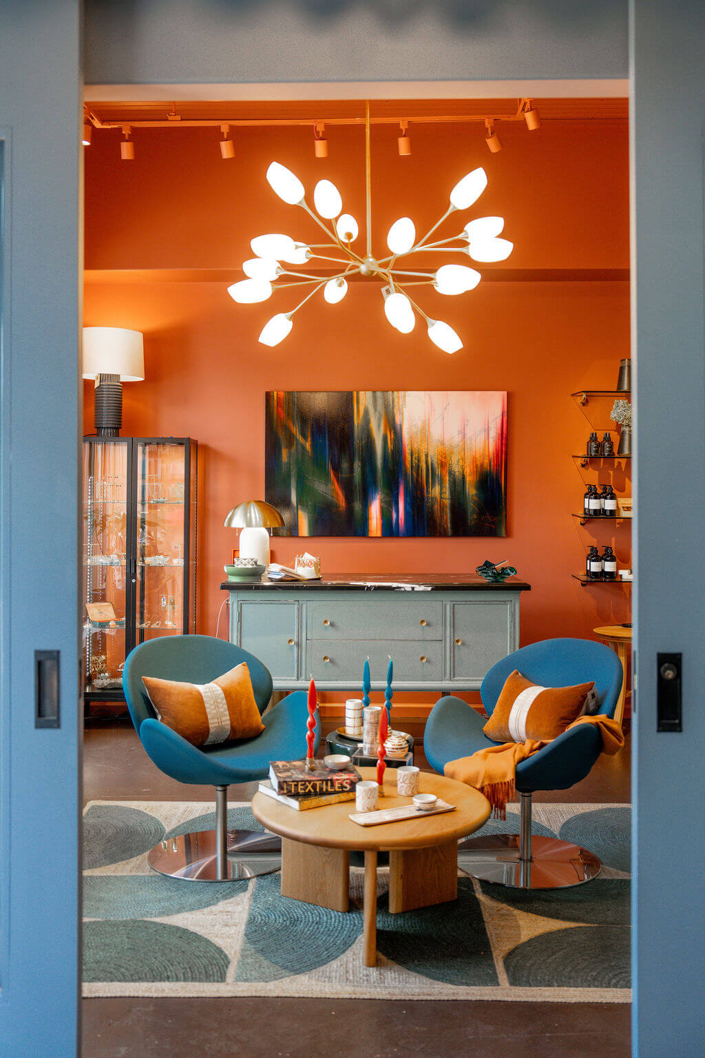 a/muse A stylish living room with orange walls, blue chairs, and a modern chandelier in Healdsburg, California.
