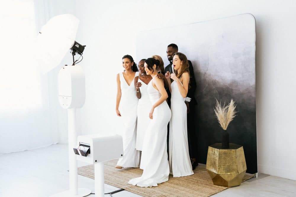 Luxe Lens, A Photo Booth Co. A group of six people in white formal attire pose for a photo in a studio setting in Healdsburg, California.