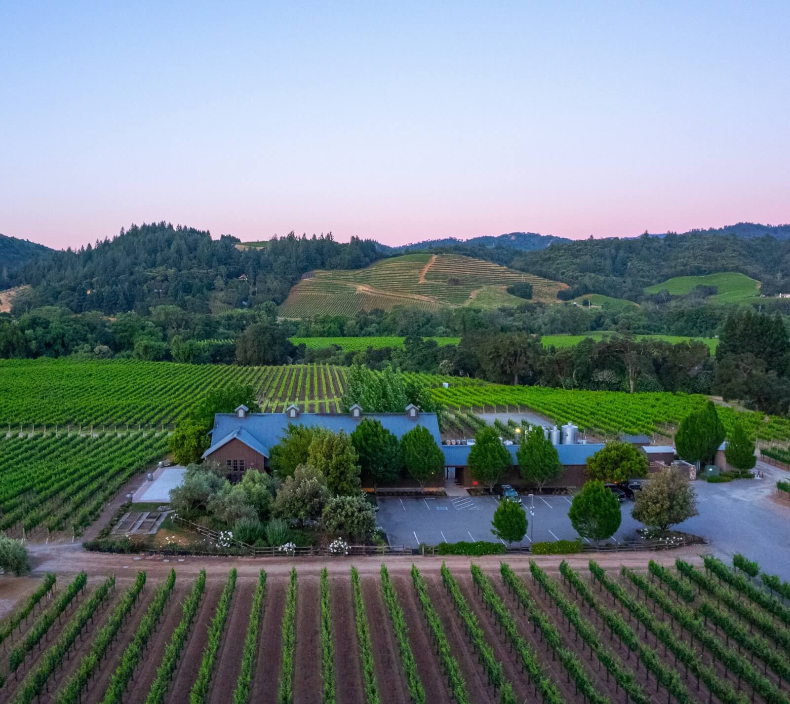 Dutcher Crossing Winery Aerial view of a vineyard with a blue-roofed building and surrounding green fields in Healdsburg, California.