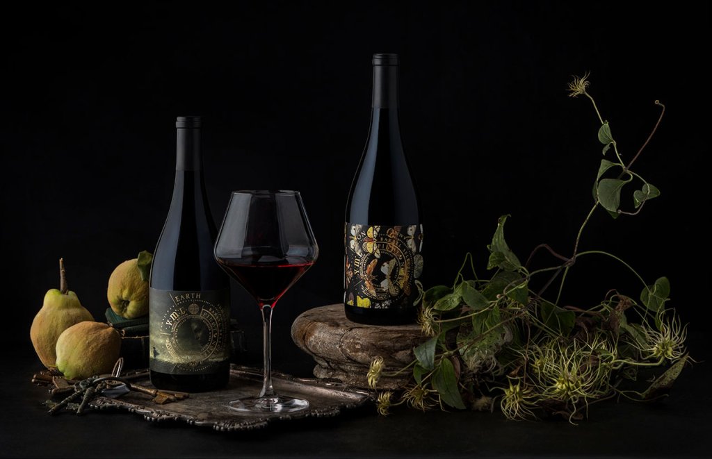 Two dark wine bottles and a glass of red wine on a tray with pears, leaves, and keys in Healdsburg, California.