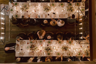An elegant, candlelit banquet with two long tables adorned with white tablecloths, floral centerpieces, and guests dressed in formal attire in Healdsburg, California.