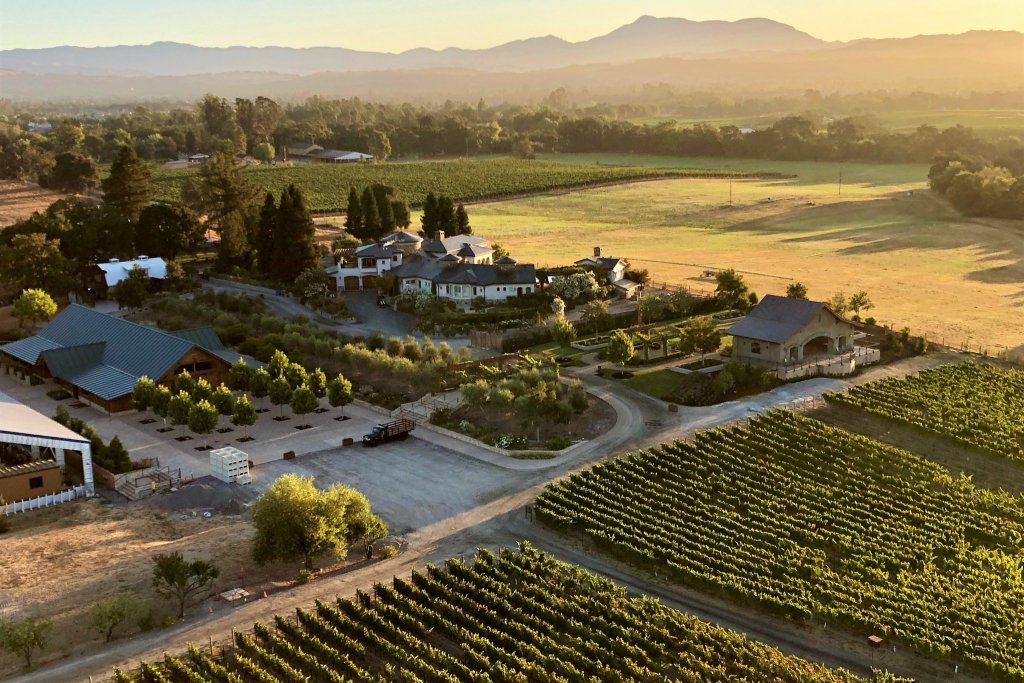 Aerial view of a sprawling vineyard with rows of grapevines, farm buildings, and a large house in Healdsburg, California.