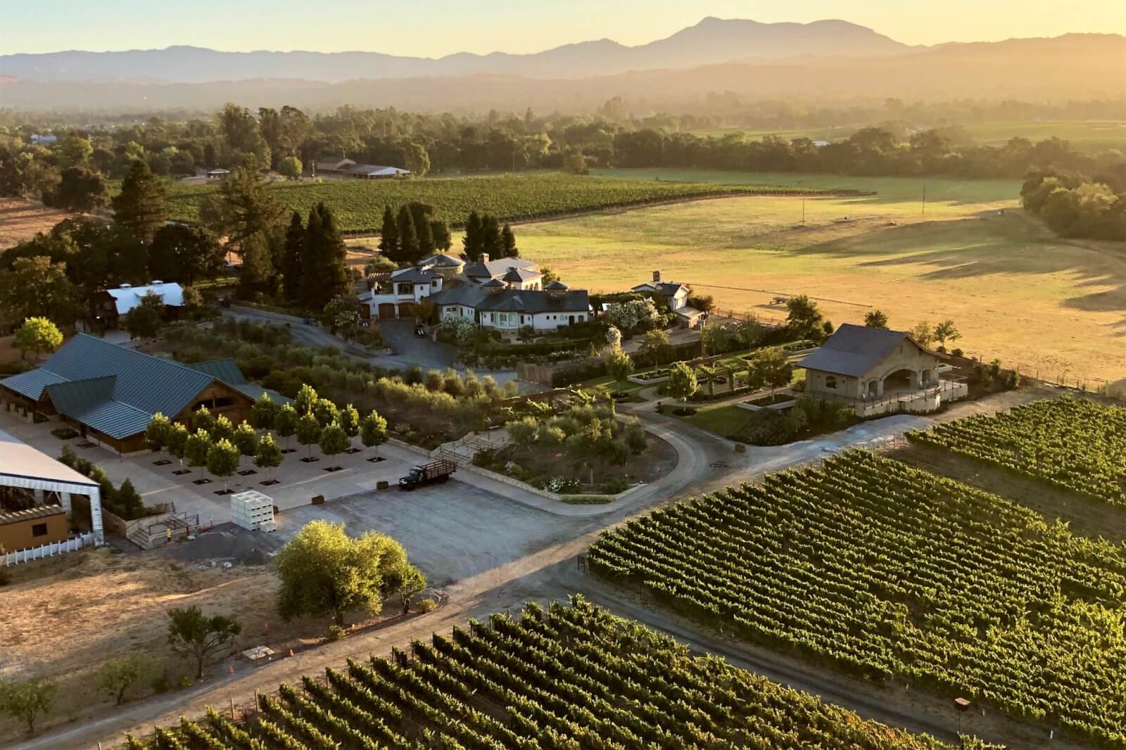 Viñedos Bricoleur Aerial view of a sprawling vineyard with rows of grapevines, farm buildings, and a large house in Healdsburg, California.