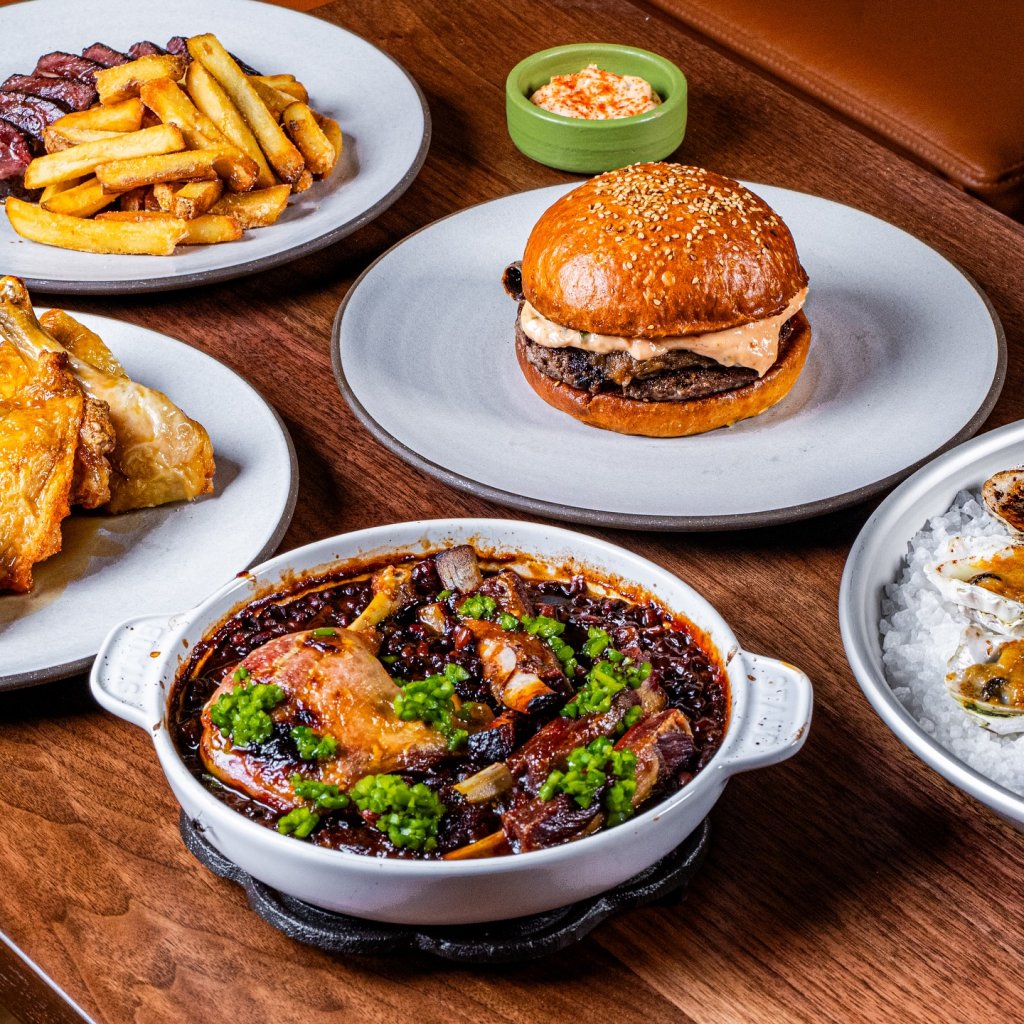A variety of gourmet dishes including a burger, chicken, steak, and seafood are arranged on a wooden table in Healdsburg, California.