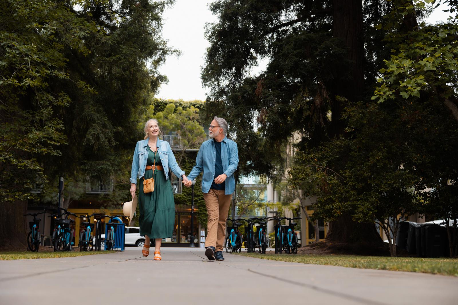 A couple walks hand in hand along a tree-lined path in a serene outdoor setting in Healdsburg, California.