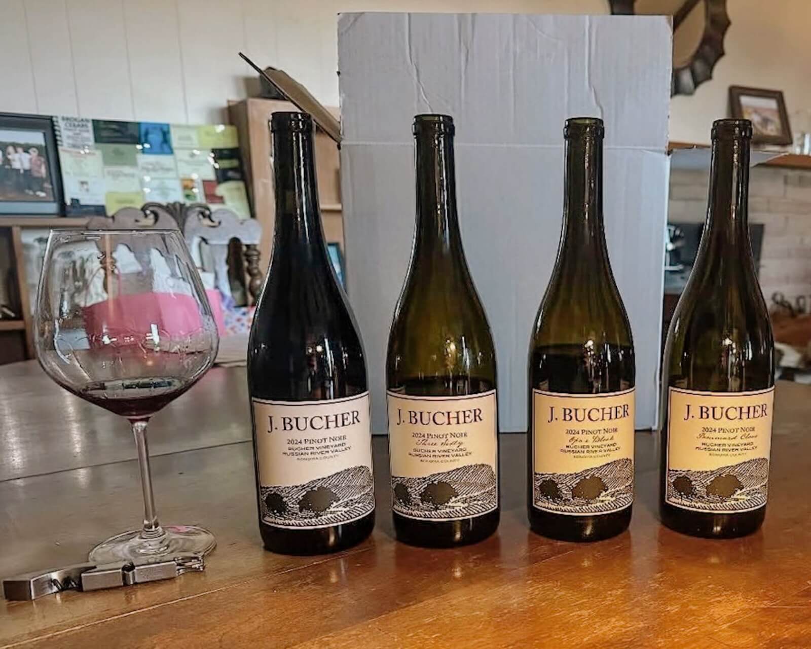 Four bottles of J. Bucher Pinot Noir wine with labels showing vineyard illustrations in Healdsburg, California.