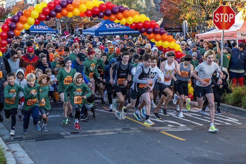 A large group of children and adults run through a colorful balloon arch in a race in Healdsburg, California.