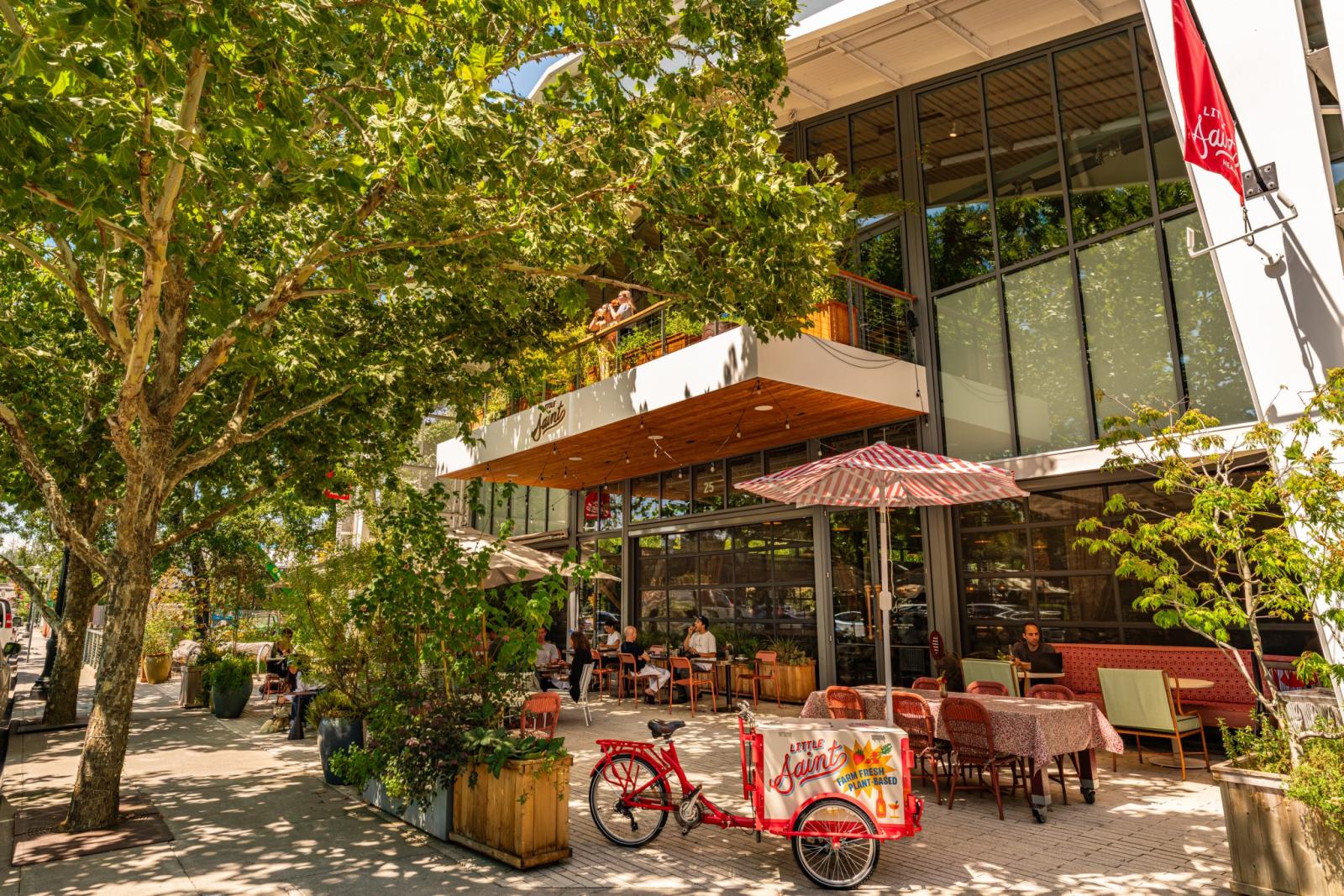 Outdoor cafe with red bicycle cart, tables, chairs, and umbrellas under trees in Healdsburg, California.