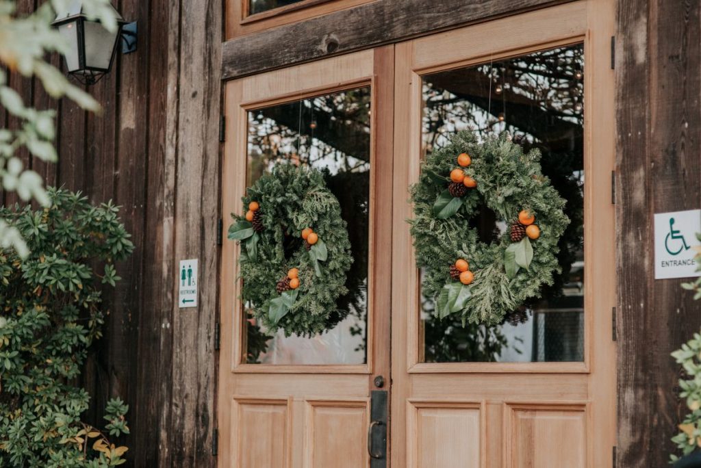Two evergreen wreaths with orange berries adorn a wooden door with glass panels in Healdsburg, California.