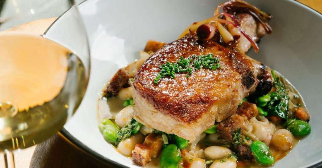 A bowl of white beans with pork chop and green vegetables, garnished with herbs in Healdsburg, California.