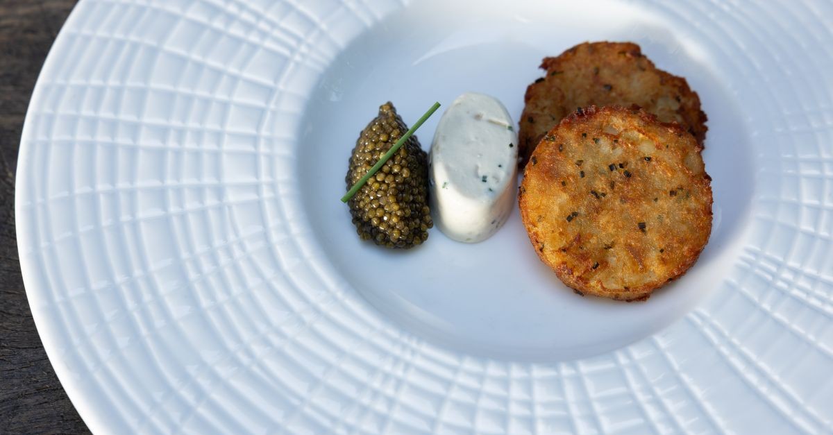 Tortitas de patata con caviar Tsar Nicoulai y champán en Dry Creek Kitchen Three round potato pancakes with caviar and sour cream on a white plate in Healdsburg, California.
