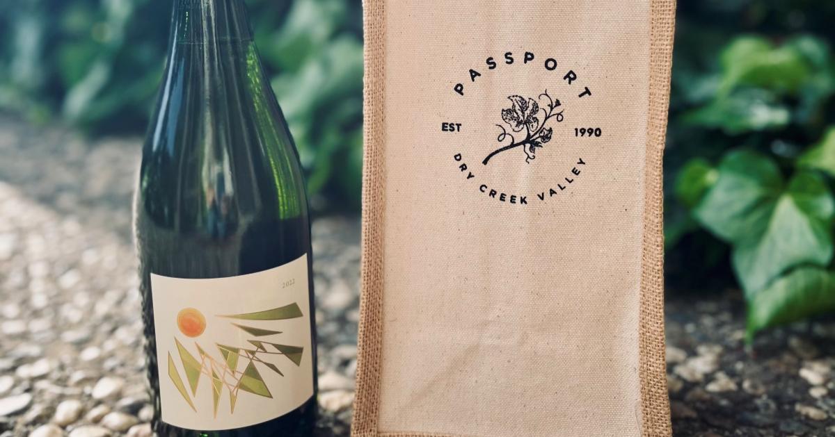 Regala un pasaporte al valle de Dry Creek. A green wine bottle with a geometric label stands next to a burlap bag with a floral logo in Healdsburg, California.