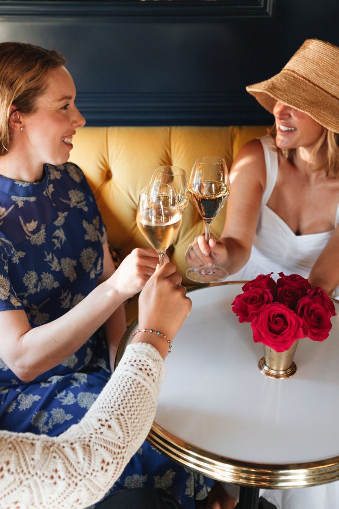 Annual Events & Holidays Three women in elegant attire raise champagne glasses in a toast at a cafe table in Healdsburg, California.