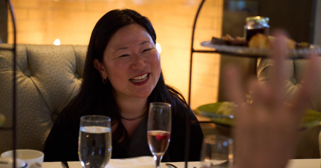 A smiling woman enjoys a meal with wine and a dessert tray in a cozy restaurant setting in Healdsburg, California.