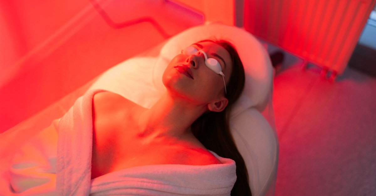 Tratamiento facial Holiday Glow en el Spa Hotel Healdsburg A woman relaxes on a spa bed, wrapped in a white towel, under red light therapy in Healdsburg, California.