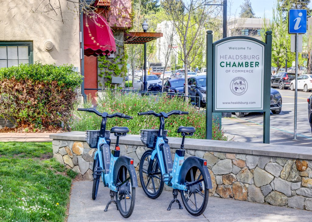 Acerca de Healdsburg, California Two blue electric bicycles parked on a sidewalk near a stone wall and a sign for the Healdsburg Chamber of Commerce in Healdsburg, California.