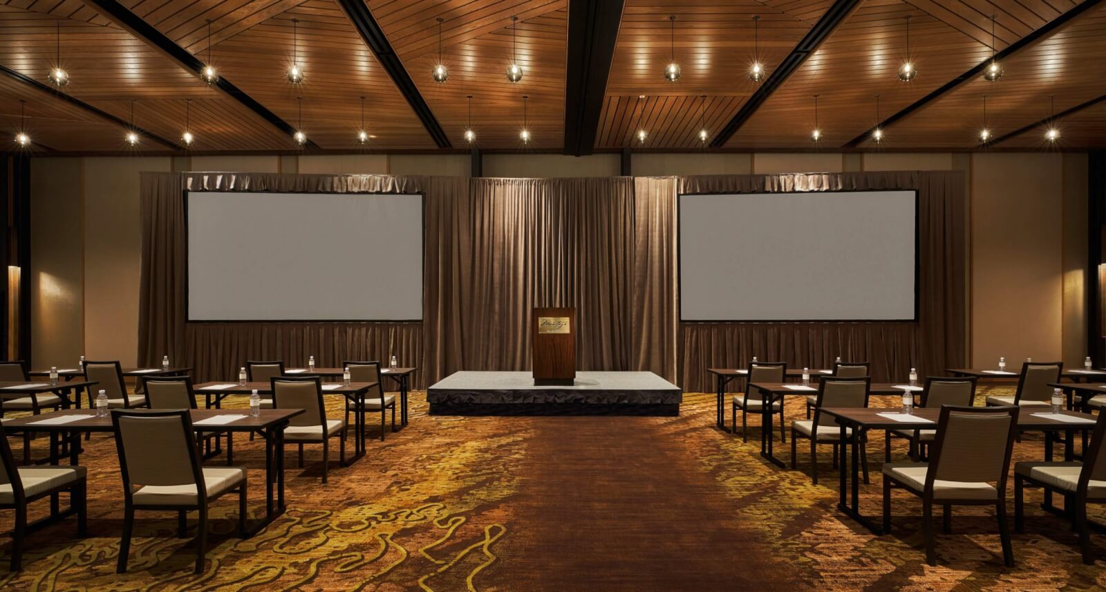 A spacious conference room with a stage, podium, and two large projection screens in Healdsburg, California.
