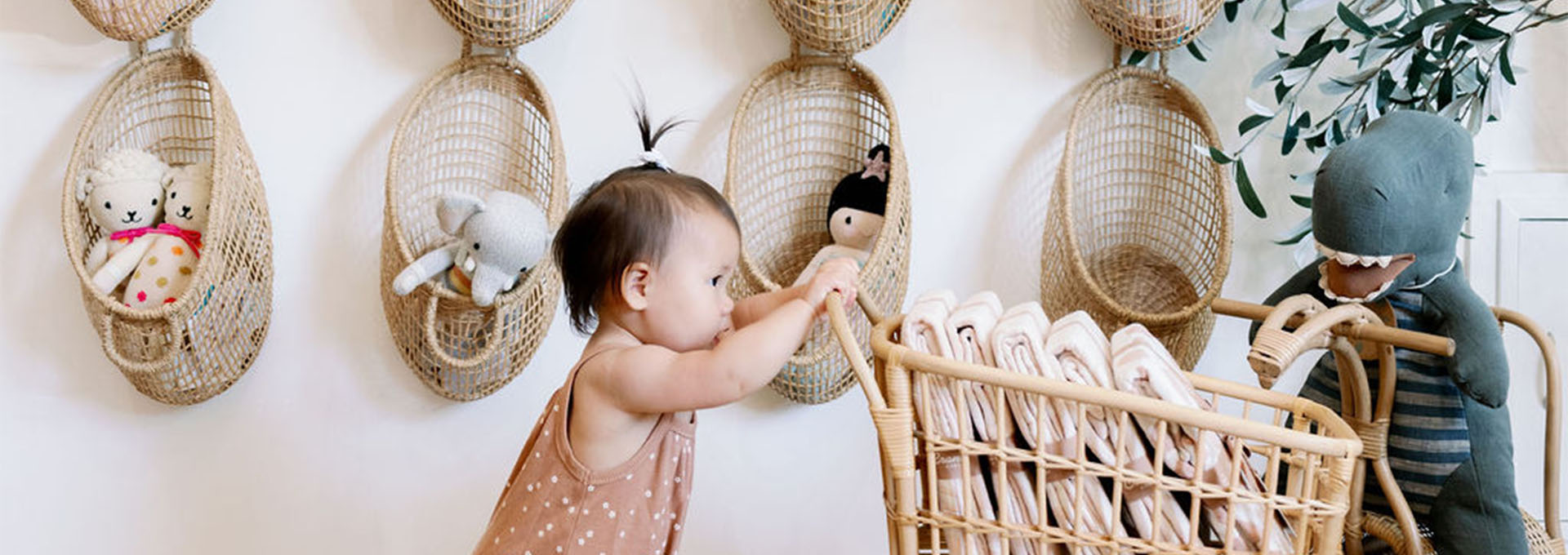A baby girl plays with a wicker cart filled with folded clothes in a nursery with hanging baskets in Healdsburg, California.