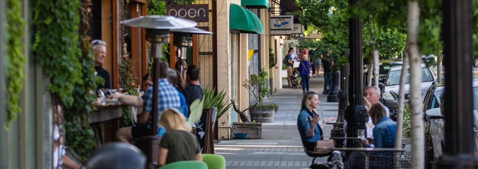 A bustling outdoor cafe scene with people dining and walking along a tree-lined street in Healdsburg, California.