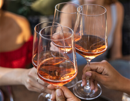 Four hands clink glasses filled with rosé wine, celebrating a joyful occasion among friends in Healdsburg, California.