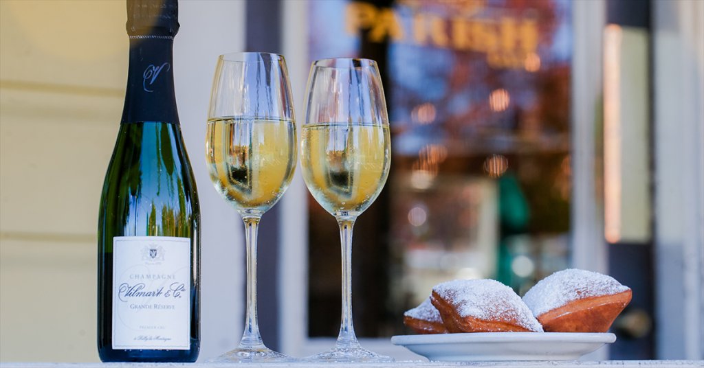 Two champagne flutes filled with bubbly wine sit beside a bottle of Champagne Ulmar & Co. on a table with three powdered sugar-coated beignets in Healdsburg, California.