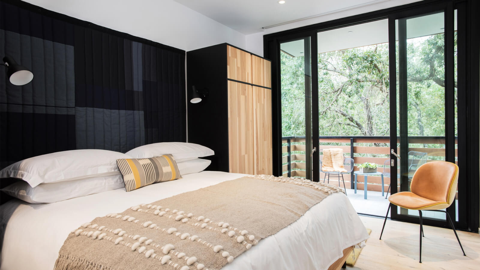 Special Offers Modern bedroom with large windows, wooden furniture, and a cozy bed with a textured throw in Healdsburg, California.