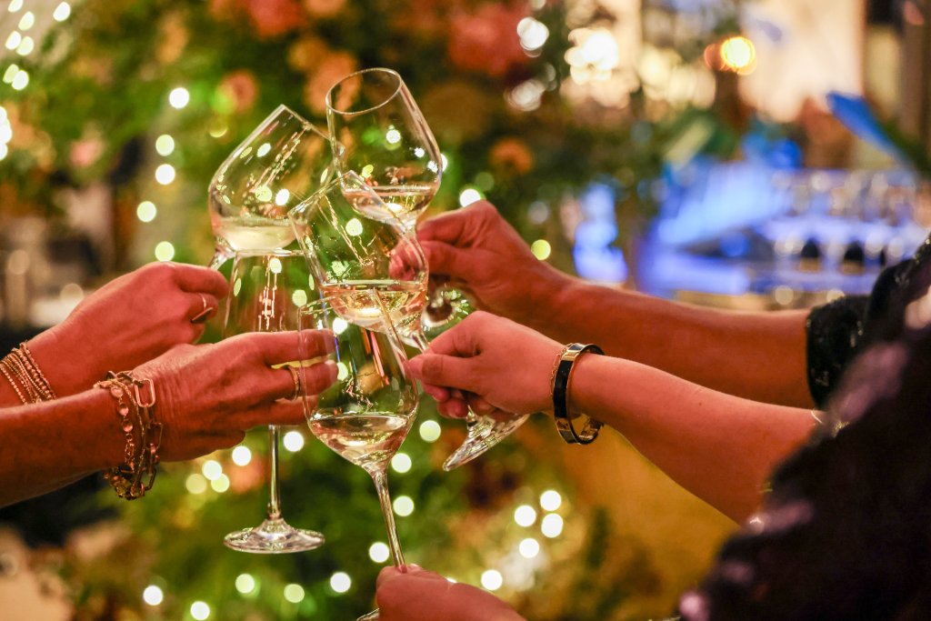 People raise glasses of white wine in a festive toast against a backdrop of Christmas lights in Healdsburg, California.